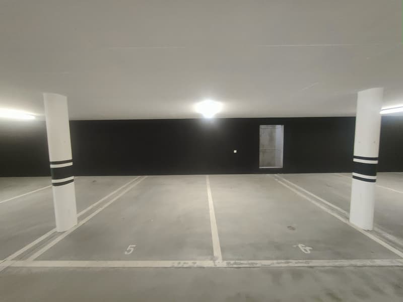 Concrete parking garage with numbered parking spaces, white lines on the floor, and a door visible in the background.