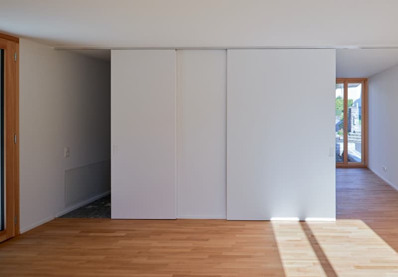 Empty room with wooden floor, white walls, sliding doors, and a glass door leading to a balcony.