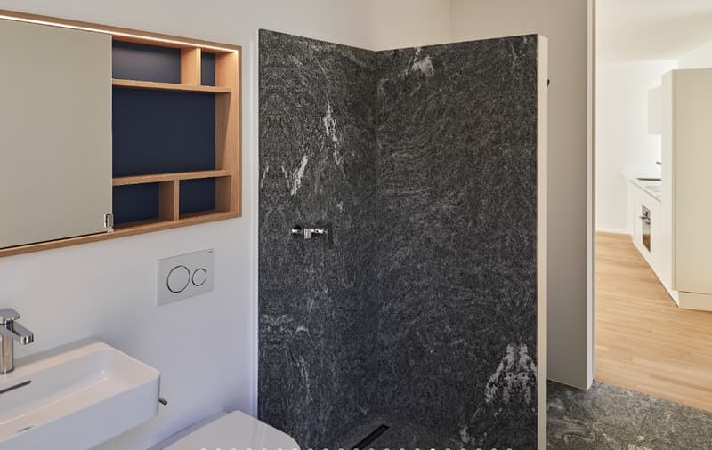 Bathroom with a white sink, a wooden cabinet, a marble wall, a toilet, and a faucet