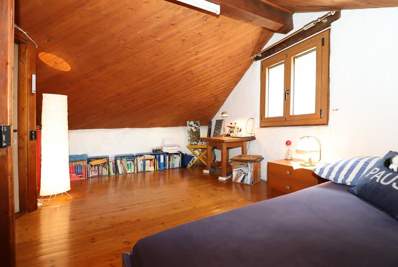Attic bedroom with wooden ceiling and walls, bookshelves, desk, and a bed with striped bedding
