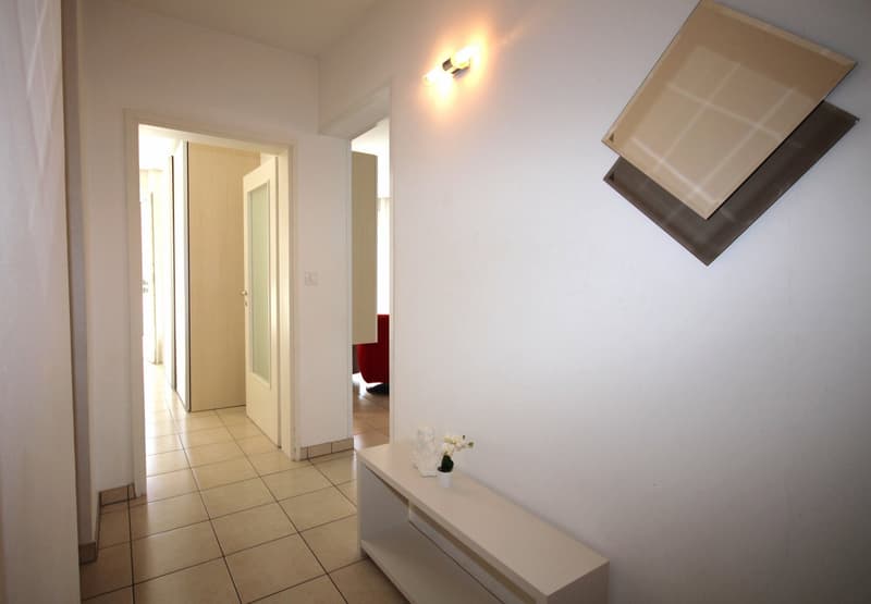 Empty hallway with white walls, tiled floor, white bench, wall art, light fixture, open doors