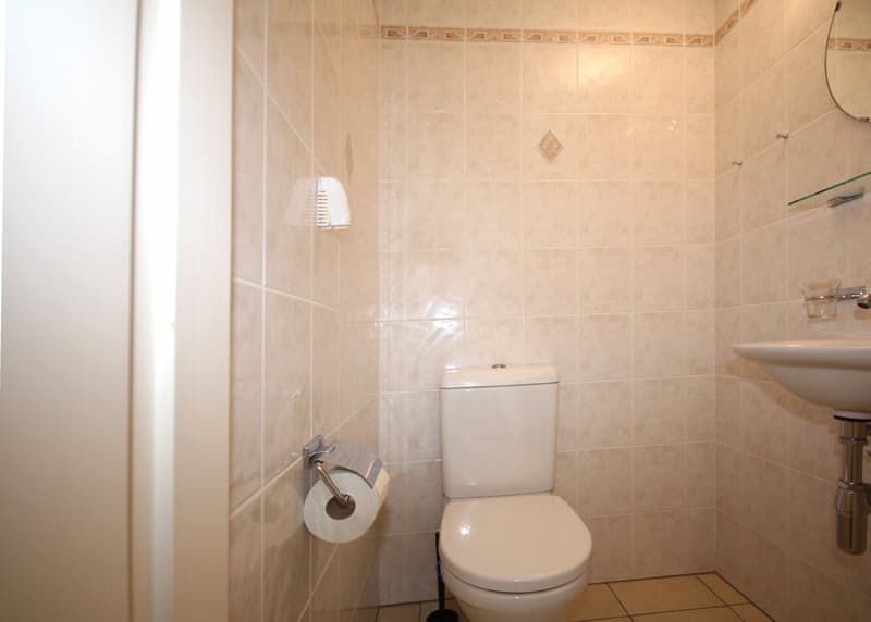 Bathroom with beige tiles, white toilet, white sink, mirror, and towel rack