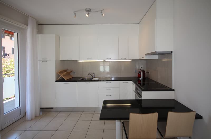 modern kitchen with white cabinets, black countertops, stainless steel sink, gas stove, and a dining table with chairs