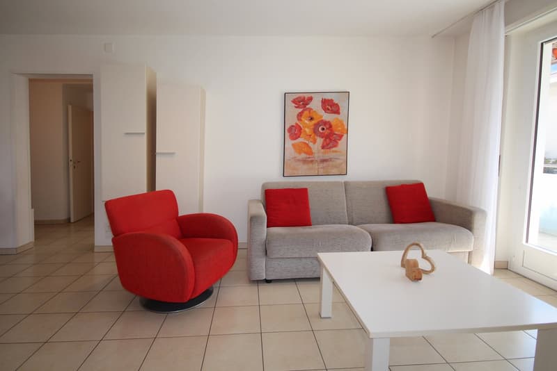 modern living room with gray sofa, red chair, white table, beige tiles, white walls, glass door, painting