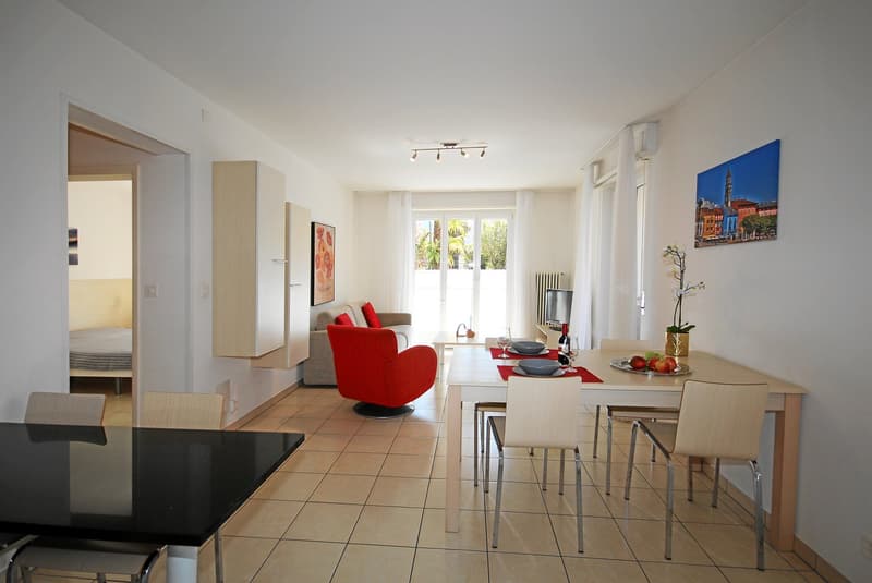 Dining area with a table and chairs, a couch, a red chair, a TV, and a painting on the wall.