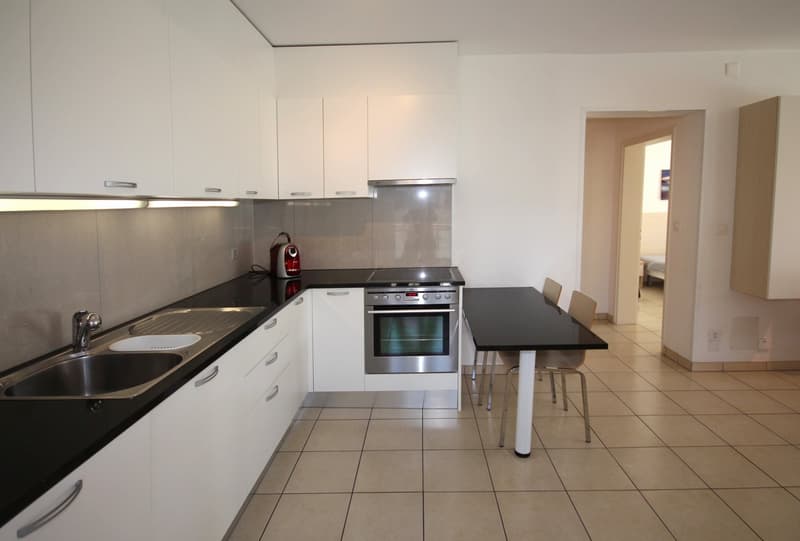 modern kitchen with white cabinets, black countertops, stainless steel sink, oven, dishwasher, and a dining table with chairs