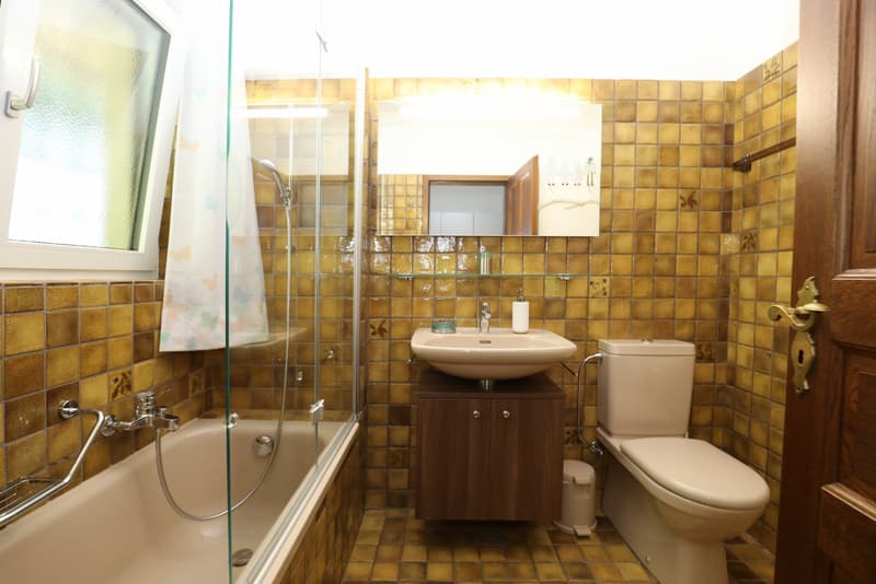 Bathroom with yellow tile walls, glass shower enclosure, vanity with sink, and toilet