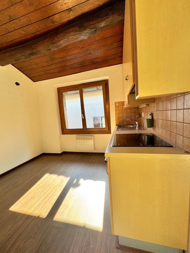 Compact kitchen with wooden ceiling beams, yellow cabinets, tiled backsplash, and a window. The kitchen appears to have a dishwasher installed.