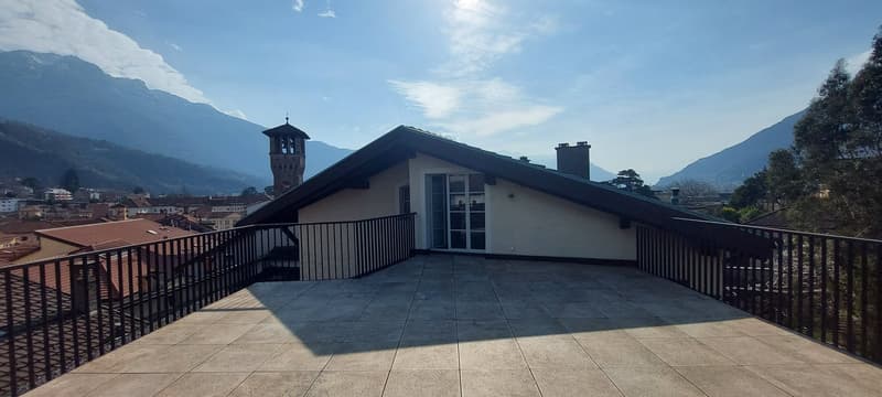 modern building with tiled rooftop, black railing on balcony, large windows, town view