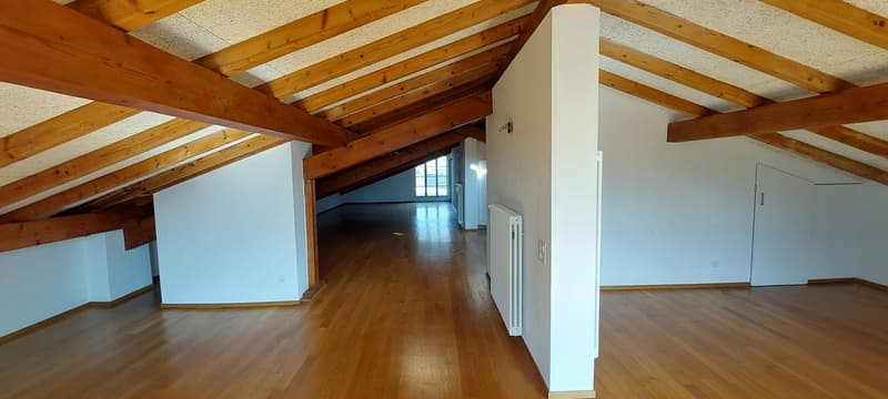 a large attic space with wooden floors and beams, white walls, two doors, and a window