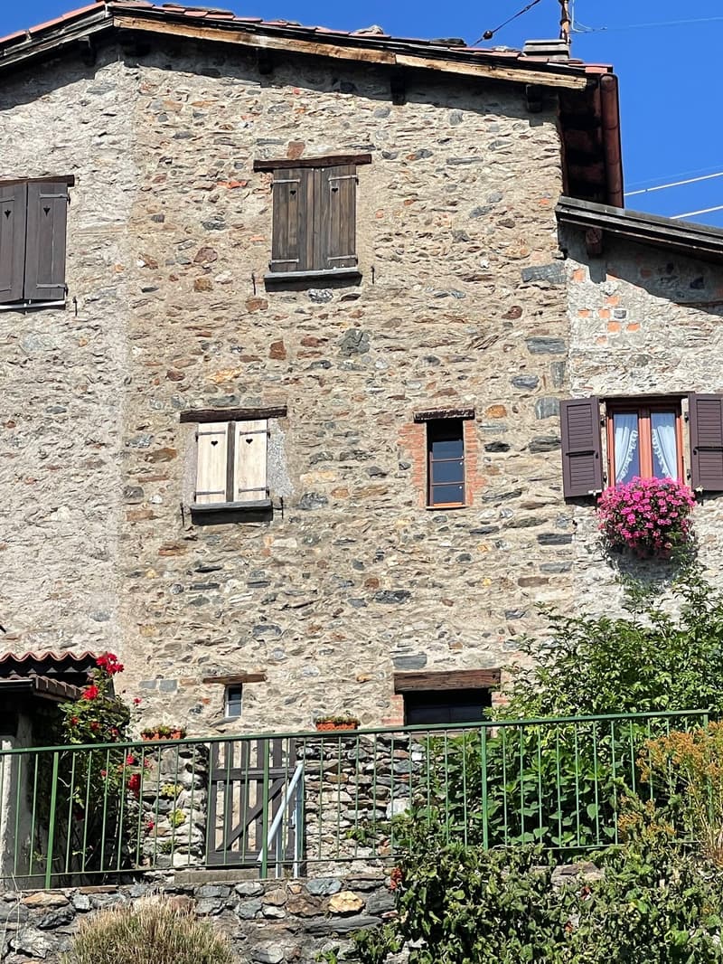 2-story stone house with wooden shutters, balcony, and flower boxes