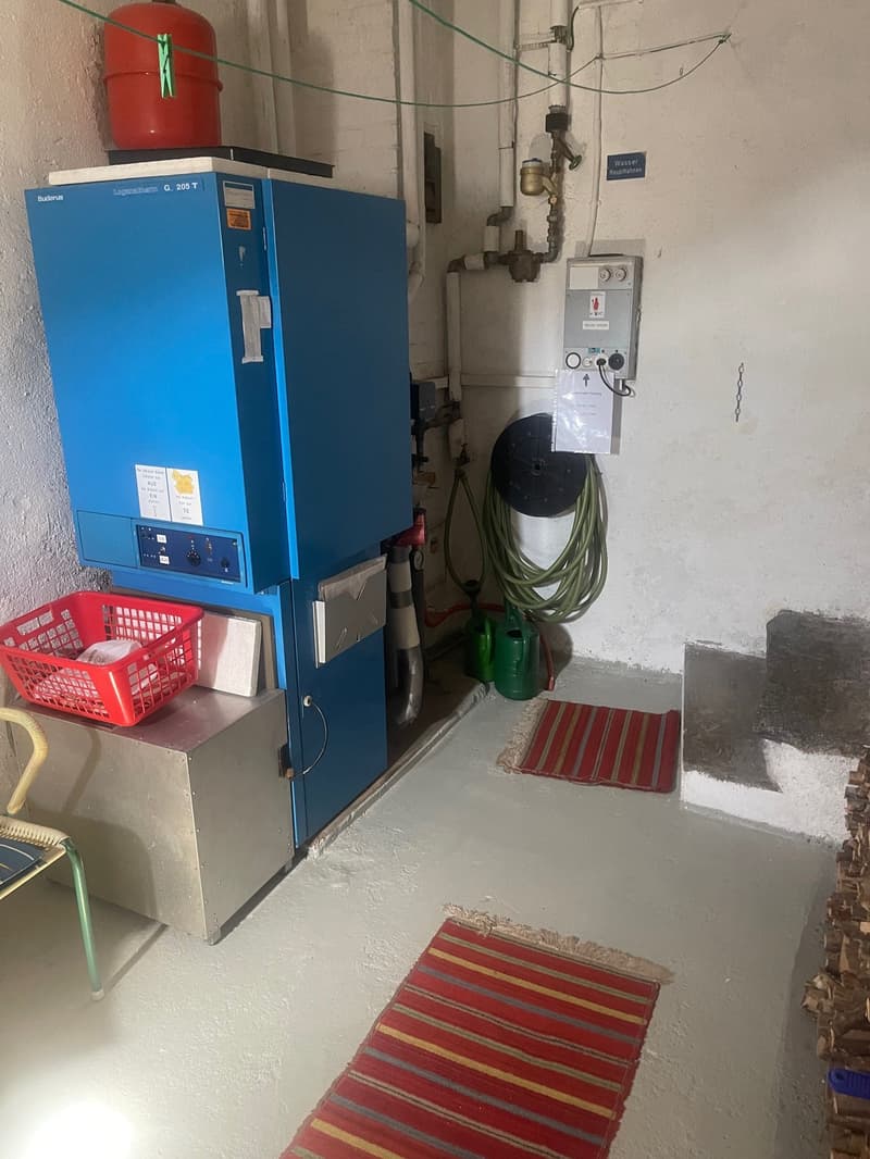 The image shows a utility room with a large blue refrigerator, a red gas canister, and various other equipment and supplies. There is a washing machine visible, indicating the presence of a private washing machine in this space.
