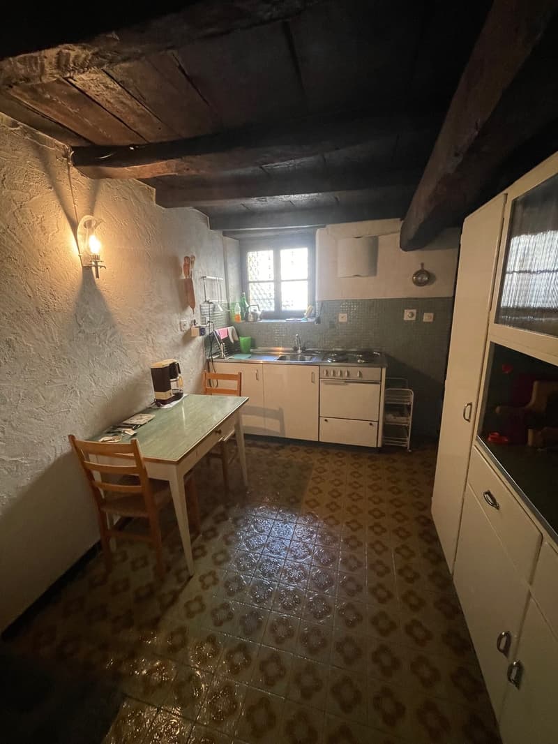 Small kitchen with wooden beams on the ceiling, tiled floor, kitchen counter with sink, stove, and appliances, small dining table
