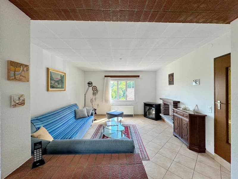 white walls, beige floor, blue sofa, coffee table, rug, fireplace, framed pictures, window with white curtains, lamp