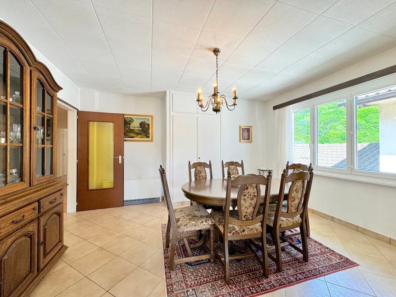 wooden dining table, chairs, chandelier, wooden cabinet, carpet, picture frames on the wall, window with white curtains