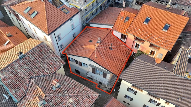 House situated in an urban setting, surrounded by other buildings. It has multiple windows and a central chimney. The building is marked with a red outline and seems to be a focal point in the aerial view.