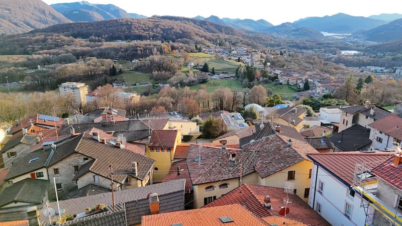 Aerial view of a village with traditional buildings, green fields, and hills in the background