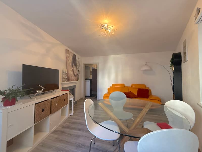 white walls, fireplace, flat screen TV, white glass table, 4 white chairs, a modern floor lamp