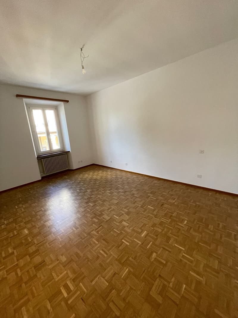Empty room with wooden floor, white walls, window, and radiator.