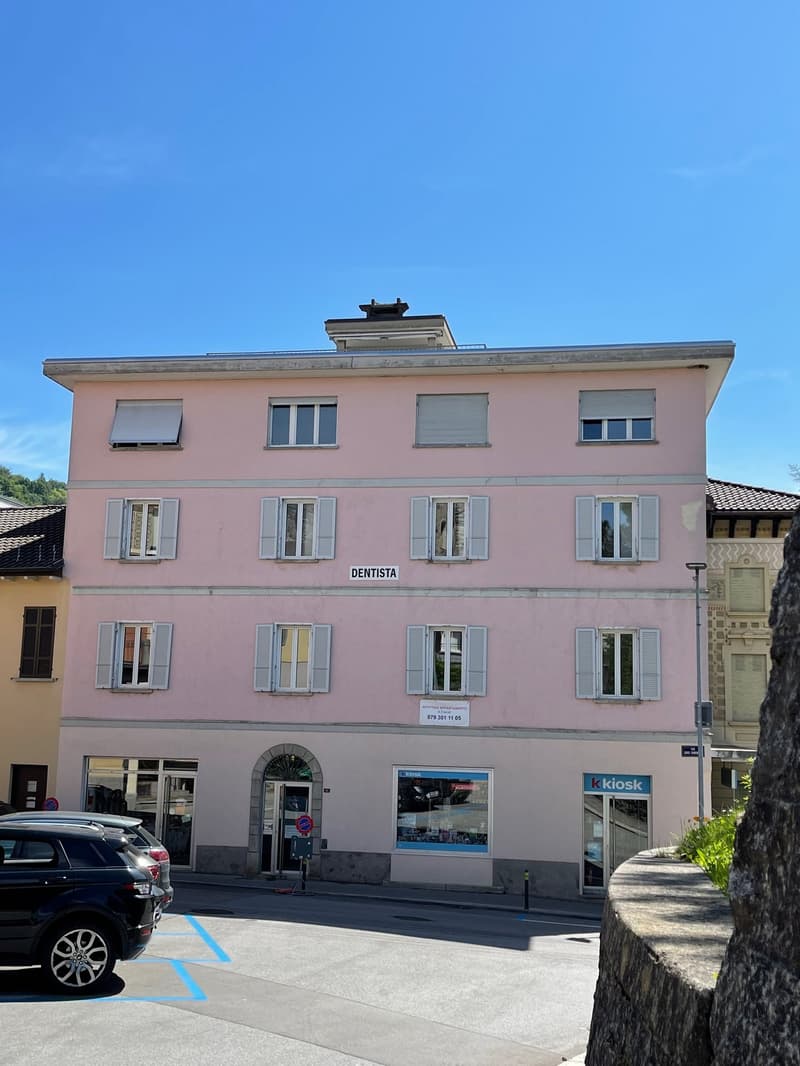 A 4-story building, pink paint, windows with white shutters, entrance with glass doors, cars parked in front