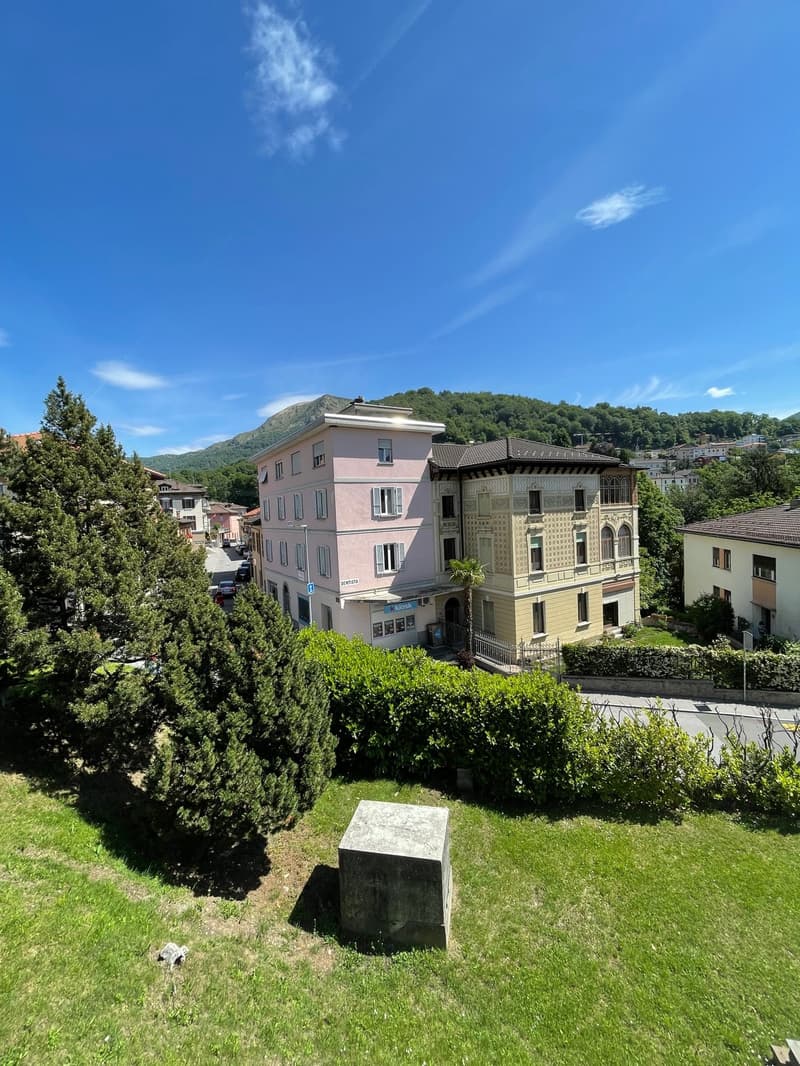 A large pink building with several windows stands in front of a mountain, with other buildings nearby.