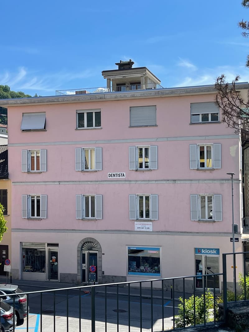 multi-unit building with multiple windows and balcony on the top, pink walls, windows with shutters, sign reading 'dentista' on the front wall, store below