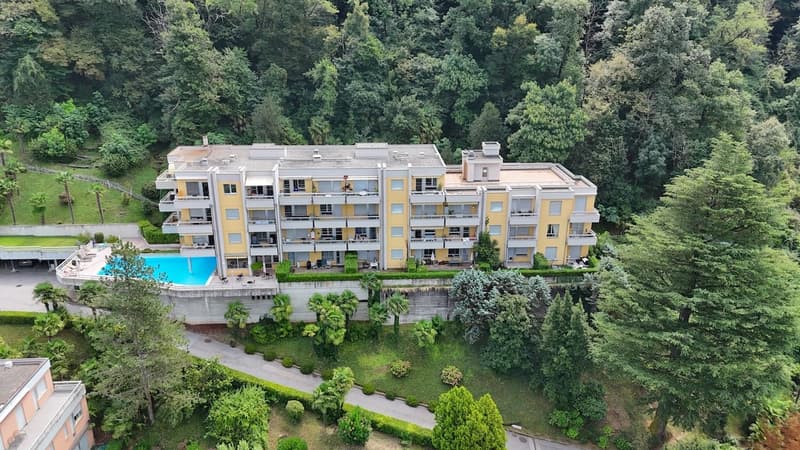 Residential building with multiple floors, yellow exterior, swimming pool at ground level, surrounded by greenery