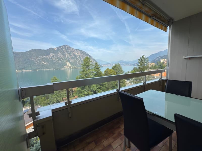 Balcony with glass railing, view of mountains and lake, dining table, 4 chairs, lamp