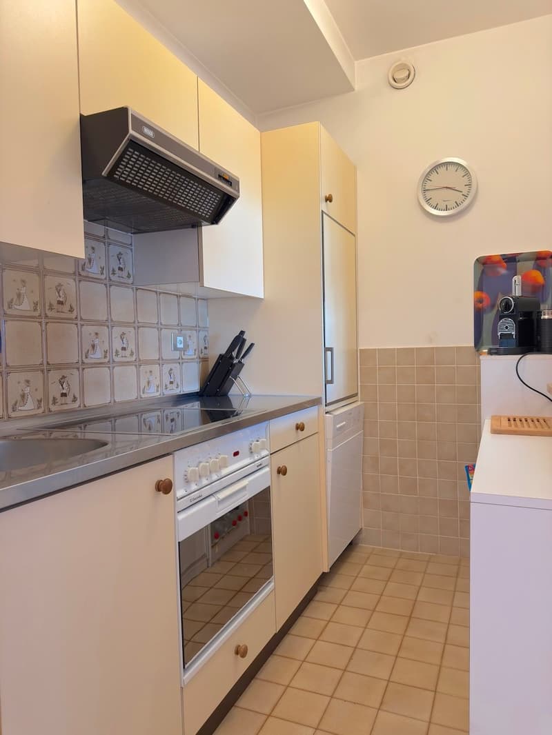 Modern kitchen with tiled flooring, white cabinetry, stainless steel countertops, white appliances, and decorative wall tiles