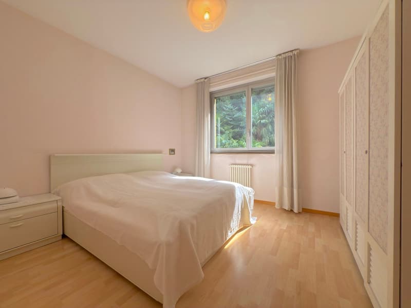 White bed, light wood floor, white nightstands, light pink walls, curtains, window, radiator