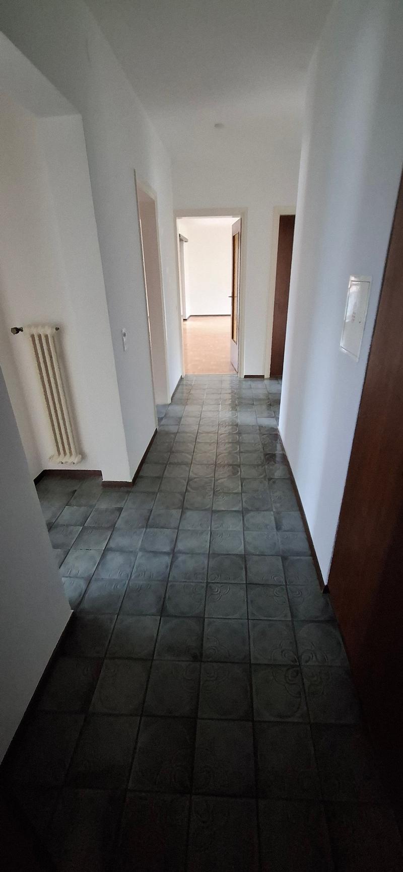 empty hallway with tiled floor, white walls, radiator, doors, and an open doorway
