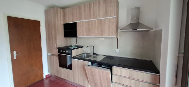 small kitchen with wooden cabinets, black countertops, silver sink, black oven, tile flooring