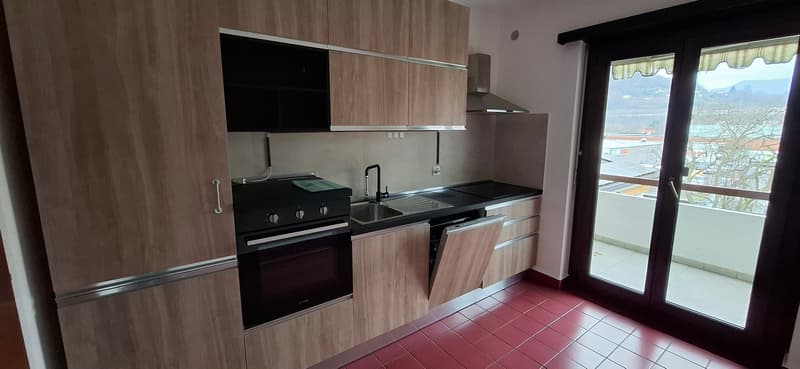Modern kitchen with wooden cabinets, red tiles, modern stove, integrated dishwasher, large windows to balcony with view