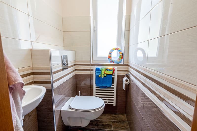 small bathroom with white sink, white toilet, white radiator, towel rack with towel, window with floater