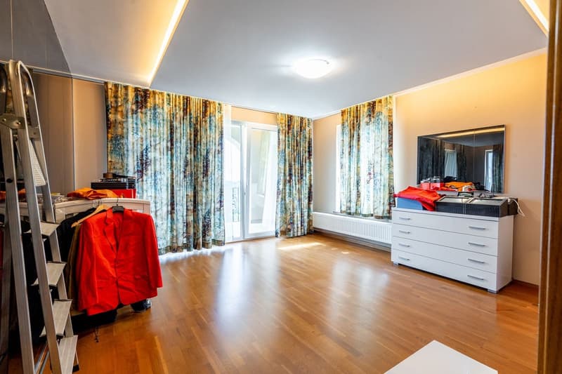 wooden floor, large windows, sliding glass door, white dresser, clothes hanging on ladder, mirror on dresser