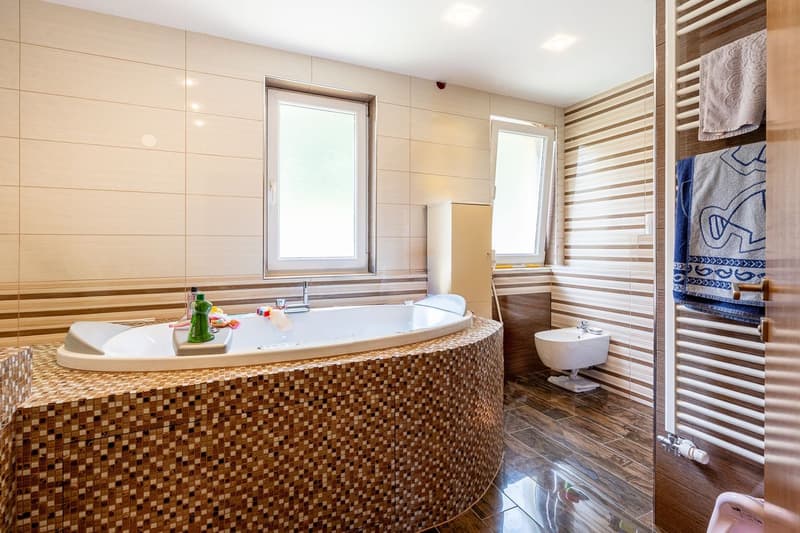 large round bathtub, white sink, white toilet, wooden floor, white and brown tiles