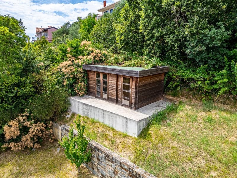 wooden shed, concrete base, surrounded by greenery, stone wall