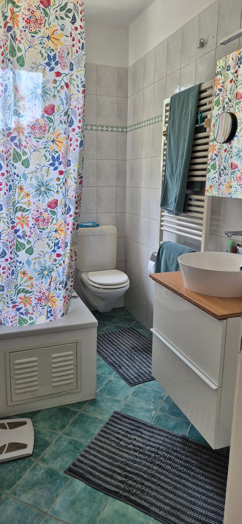 Bathroom with white bathtub, white toilet, white sink, green tiles, towels on the towel rack, floral shower curtain