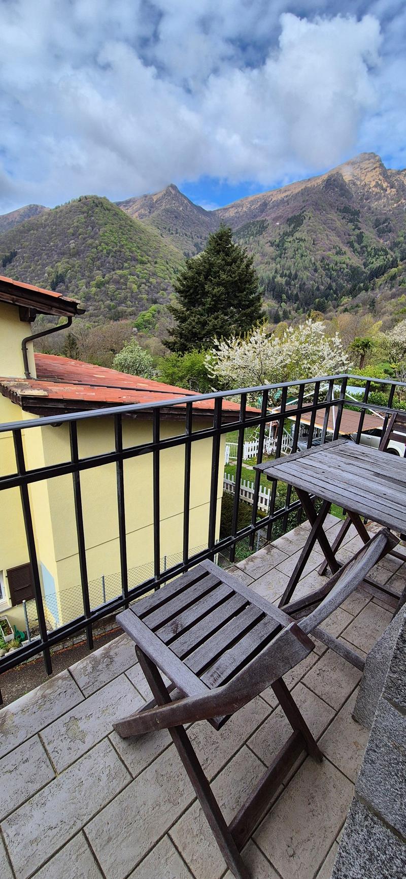 Balcony with wooden table and chairs, black railing, tiled floor, view of mountains