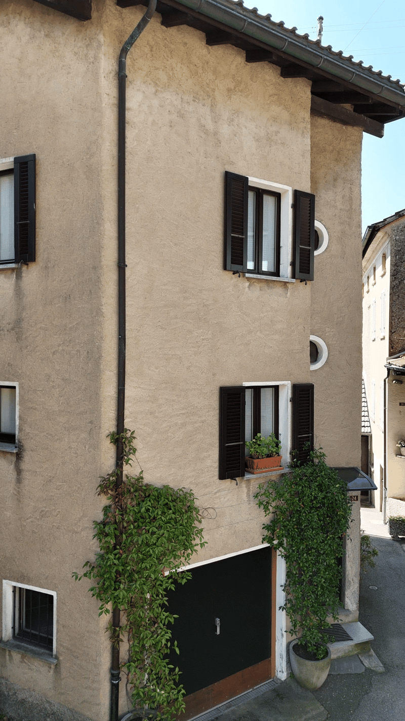 3 story house, beige exterior, black shutters, black garage door, plants on the wall