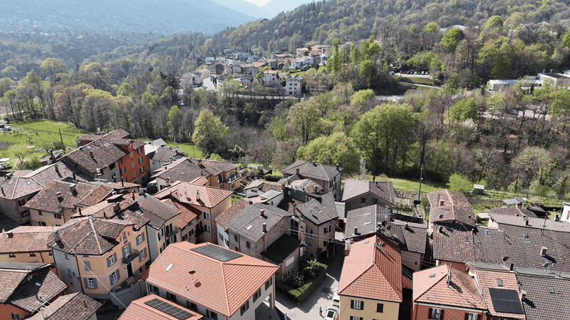 Aerial view of a town with many houses, some with solar panels on the roofs, surrounded by trees and mountains
