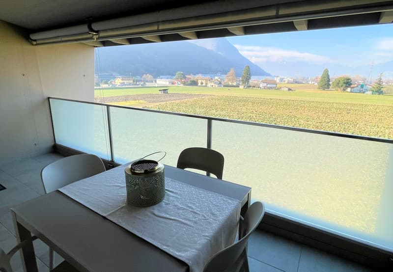 Dining area with a table and chairs, large glass windows, balcony, view of a field and mountains
