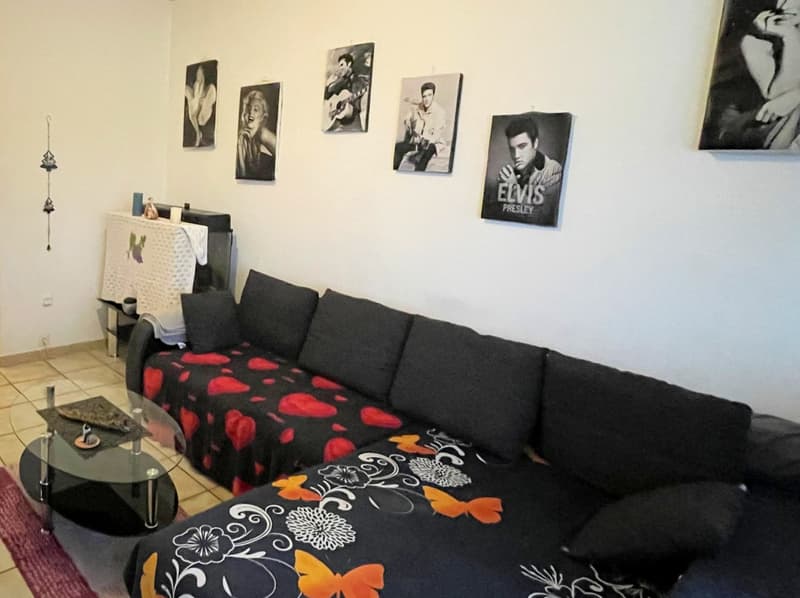 living room, white walls, black couch, decorative items, six picture frames, glass table, tiled floor, red rug