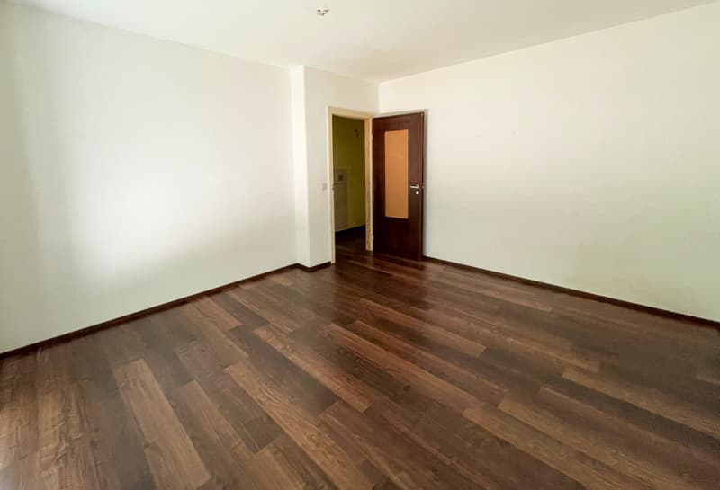 Empty room with wooden floor, white walls, open door, small hallway