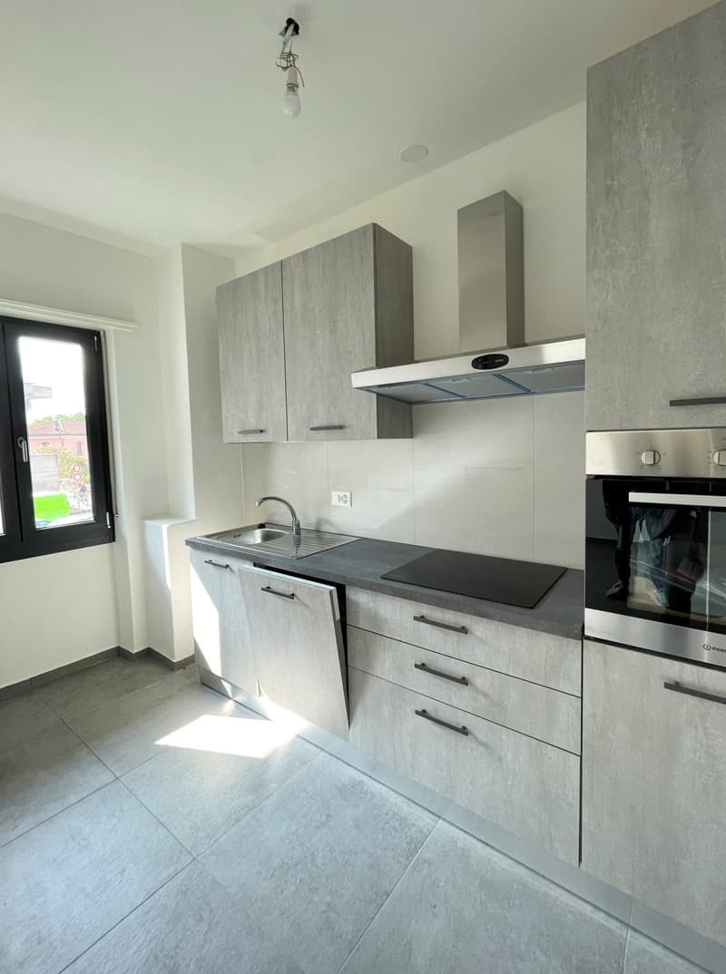 Modern kitchen with white walls, stainless steel countertop, oven, sink with faucet, and tiled floor