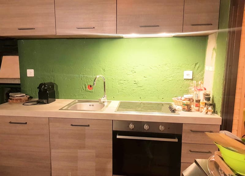 Wooden cabinets, white countertop, green wall, kitchen sink, stove, oven, appliances on the counter