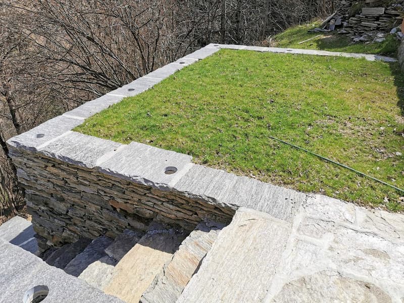 stone wall, grassy area, concrete base, outdoor stairs, distant trees