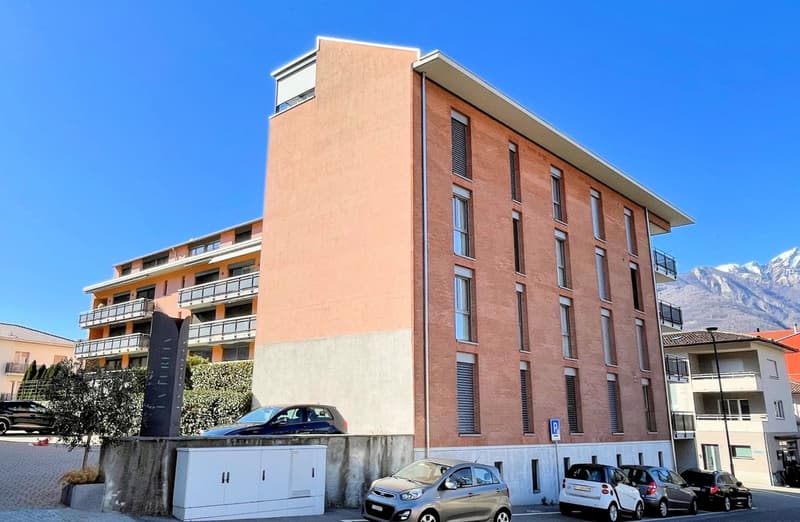 A two-story building with a parking space in front, brick wall, parking lot, car parked, white cabinets, trees, and balcony