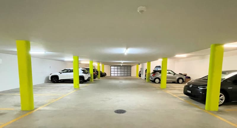 A parking garage with several yellow pillars, ceiling lights, and parked cars