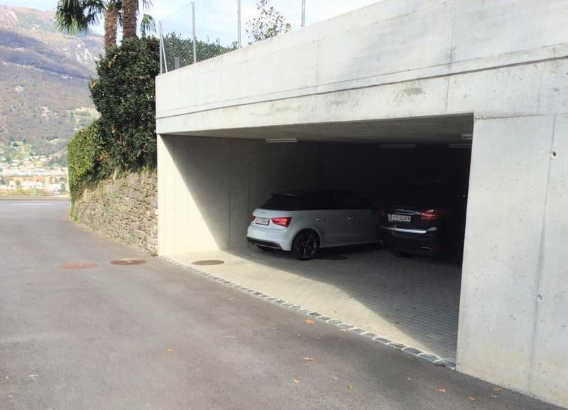 Parking space with concrete structure and two cars parked, surrounded by paved road and greenery